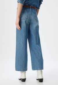 Jeans de tiro alto y pierna ancha de color azul hechos de denim, con bolsillos traseros y un cinturón con un acento marrón. Textura suave con un ajuste relajado.