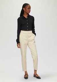 Black long-sleeve button-up shirt, cream tailored pants, and black flats. The shirt features a classic collar and buttons down the front.