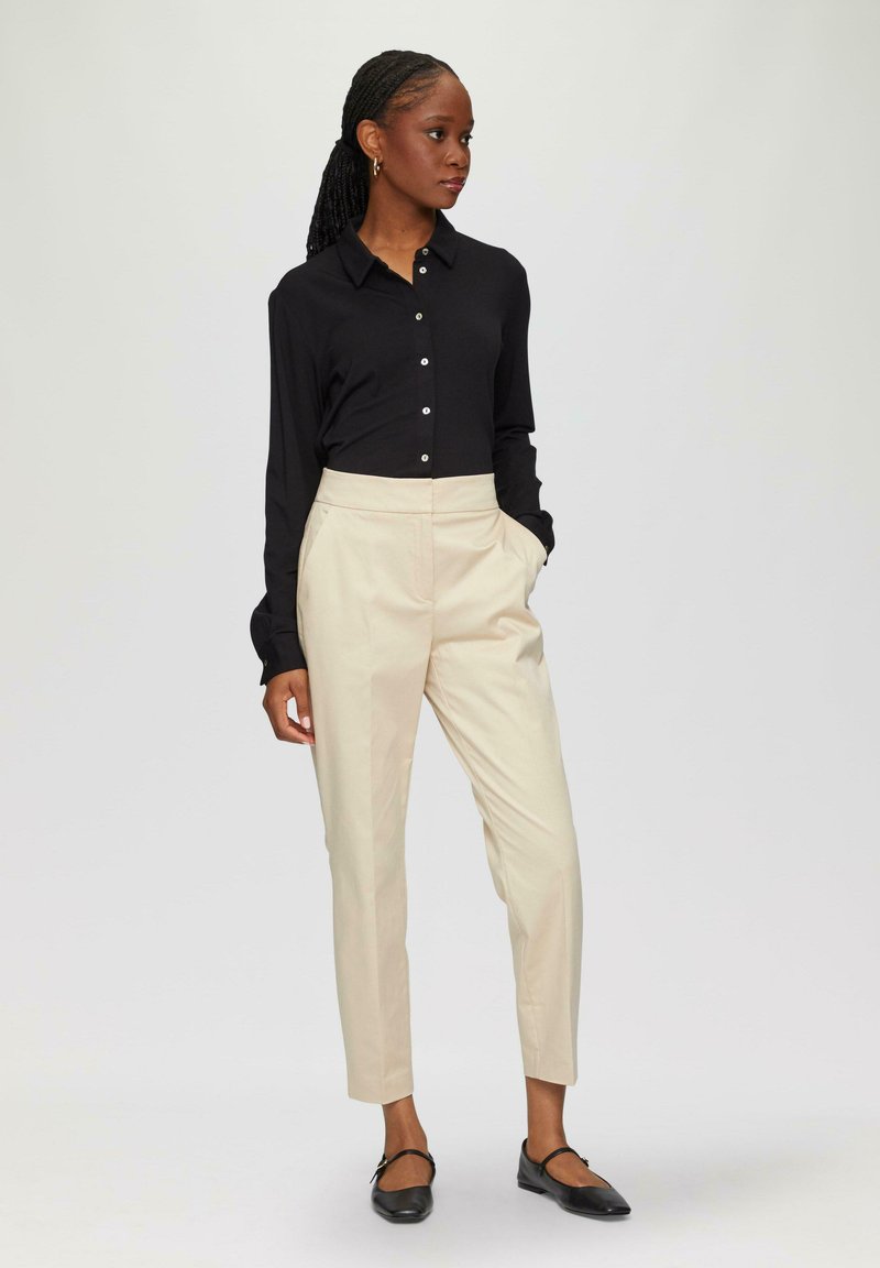 Black long-sleeve button-up shirt, cream tailored pants, and black flats. The shirt features a classic collar and buttons down the front.