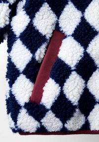 Jūras spēku un balti dimanta raksti flīsa audums ar mīkstu, struktūrētu virsmu; sarkans akcenti redzami kabatā.