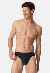 Slip da nuoto neri con righe verticali bianche, caratterizzati da un design a vita bassa e una cintura elastica per una vestibilità aderente.