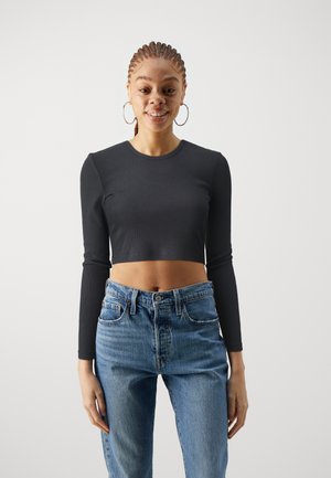 Black cropped long-sleeve top with a ribbed texture, paired with high-waisted blue denim jeans. Simple round neckline and fitted design.