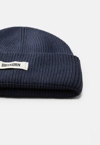 Berretto a costine in maglia di colore navy con risvolto e un'etichetta bianca con il logo "DRYKORN". Texture morbida, spessore medio.