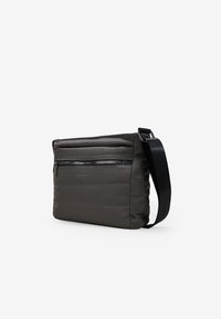 Bolso cruzado de color gris oscuro, confeccionado en una tela suave con textura acolchada, que cuenta con un bolsillo frontal con cremallera y una correa negra ajustable.