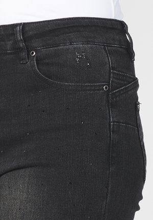 Jean en denim noir avec une coupe slim, des détails subtilement usés, des accents brillants et un design classique à cinq poches.
