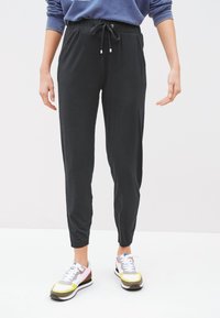 Black tapered jogger pants with a drawstring waist, side pockets, and soft fabric texture, styled with colorful athletic shoes.