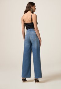 Jeans in denim blue a gamba larga con vita alta, caratterizzati da un design a cinque tasche e un'etichetta in pelle sulla parte posteriore della vita. Abbinati a un top nero.