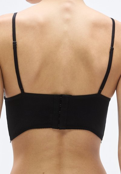 Čierna bandeau podprsenka s nastaviteľnými ramienkami, bezšvovým dizajnom a zapínaním na háčiky vzadu. Hladká textúra bez viditeľných vzorov.
