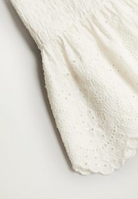 Tissu en coton blanc avec un détail en broderie anglaise texturée, présentant un corsage smocké et des bords festonnés.