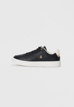 Black leather sneaker with white sole, featuring gold eyelets and logo. Smooth texture, low-top design, and contrasting heel accent.