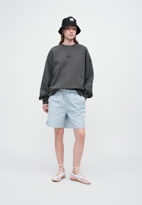 Sudadera gris de gran tamaño, pantalones cortos de patrón azul claro, sombrero de cubo negro y zapatos rosa claro con cordones y acentos blancos. Conjunto simple y casual.