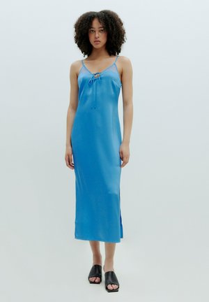 Blauwe satijnen slipdress met dunne bandjes, kantaccenten, een strikdetail bij de hals, een zijsplit en een knielange zoom. G gecombineerd met zwarte slide sandalen.
