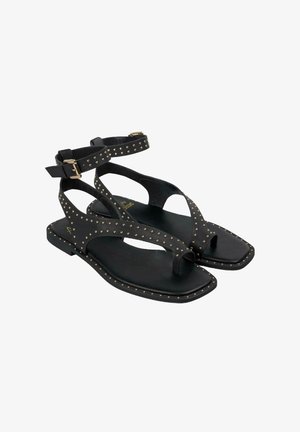 Sandali neri flat con dettagli a borchie, cinturino alla caviglia con fibbia e design T-bar con punta aperta e soletta testurizzata.