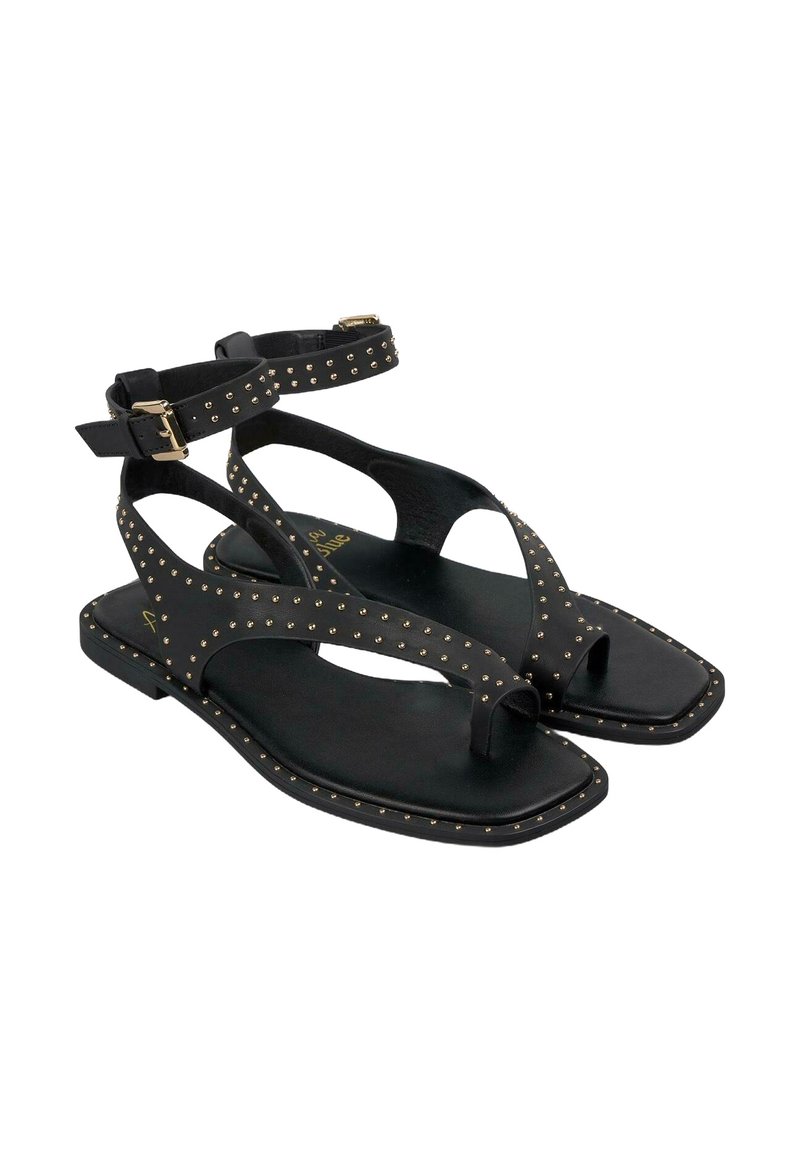 Czarne płaskie sandały z ćwiekami, z paskiem na kostkę z klamrą oraz designem T-bar, z odkrytymi palcami i teksturowaną wkładką.