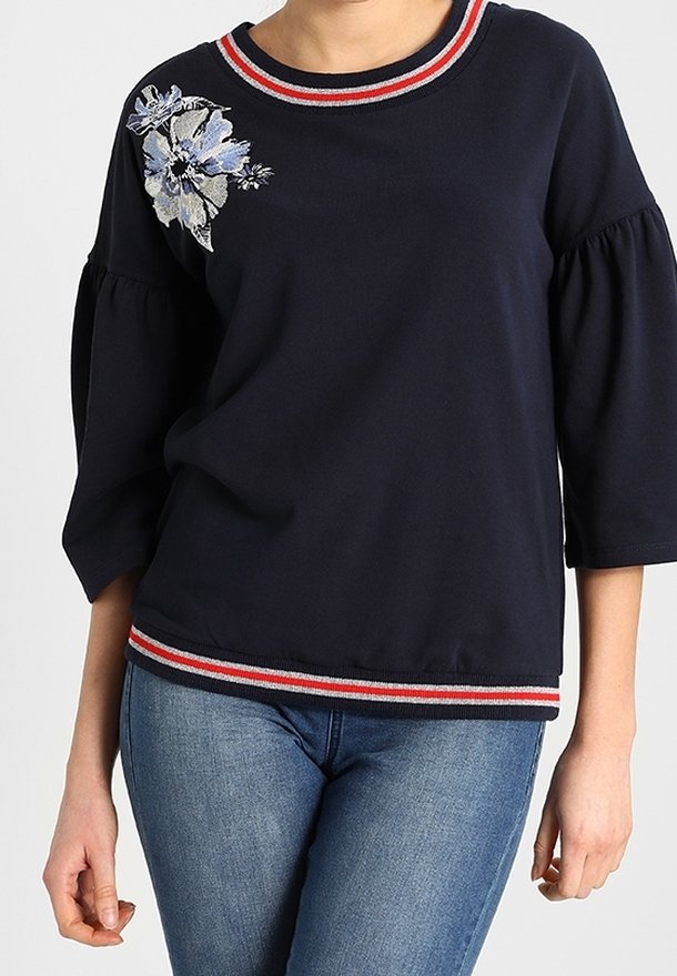 Felpa blu navy con maniche a tre quarti, colletto e fondo a righe rosse e bianche, caratterizzata da ricami floreali sul lato sinistro.