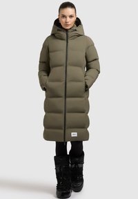 Manteau rembourré long vert olive avec capuche, fermeture éclair devant et deux poches latérales. Accents noirs et logo visibles à l'ourlet.