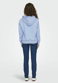 Lys blå hoodie med snoretræk i hætten, ribbede manchetter og kant. Kombineret med mørkeblå jeans og hvide sneakers. Vist fra bagsiden.