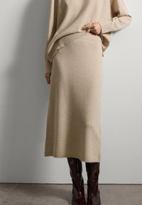 Suéter de punto beige y falda midi a juego, textura suave, acentos acanalados, combinados con botas altas de charol burdeos.