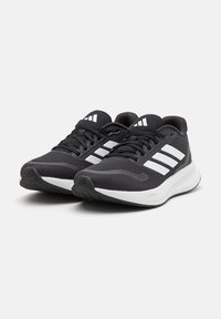 Paire de chaussures de course athlétiques noires et blanches avec trois bandes blanches et des lacets noirs sur fond blanc.