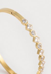 Bracciale in oro con cristalli trasparenti alternati di forma rotonda e a diamante. Texture metallica liscia con un design a chiusura a cerniera.