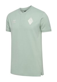 Jasnozielona polo z krótkim rękawem i kołnierzykiem, ozdobiona białym emblematem oraz subtelnymi rozcięciami po bokach, które zapewniają swobodę ruchów. Wykonana z miękkiego materiału.