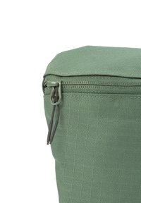 Nahaufnahme einer grünen Stofftasche mit Reißverschluss, die eine strukturierte Oberfläche und einen Reißverschlussgriff für einfaches Öffnen aufweist.