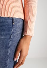 Ljust rosa ribbat stickad tröja med långa ärmar, kombinerad med mörkblå jeans. Fokusera på texturen av tröjan och tygdetaljer.