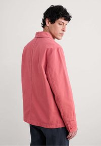 Chemise en coton rose avec une coupe décontractée, poignets boutonnés et col classique. Texture lisse et design minimaliste.