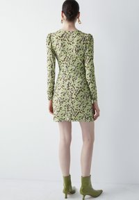 Robe mini à imprimé floral vert avec des manches longues et des détails froncés, associée à des bottines vertes brillantes. Texture de tissu lisse.