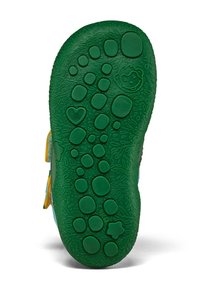Suola verde di una scarpa da bambino con motivi rialzati a forma di cerchio, cuore, stella e faccia di scimmia per la presa e un design giocoso.