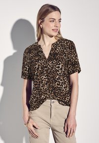 Blusa a maniche corte con stampa leopardata in tonalità marrone e nera, con scollatura a V e vestibilità comoda, abbinata a pantaloni beige chiaro.