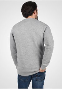 Grey ribbed sweatshirt with long sleeves, round neckline, and textured surface, paired with blue denim jeans.