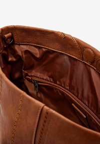 Braune Lederhandtasche mit einem glatten, glänzenden Innenfutter und einer Reißverschlusstasche; mit sichtbaren Nähnähten und abgerundeten Akzenten.