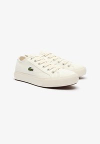 Lacoste spordijalatsid off-white kangast, metallist silmadega, ümar nina, tekstuuriga tallaga ja rohelise logoga külgedel.