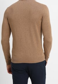Pull marron en tricot avec manches longues, poignets et ourlet côtelés, coupe ajustée, texture lisse et col rond.