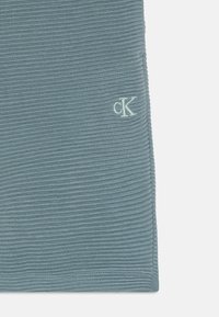 Textúrált világoskék anyag, függőleges bordázással és egy kis hímzett "cK" logóval. Az anyag puhanak és rugalmasnak tűnik.