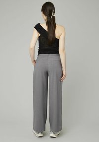 Top noir à une épaule en tissu texturé associé à un pantalon large gris clair avec une coupe ajustée et des poches arrière.