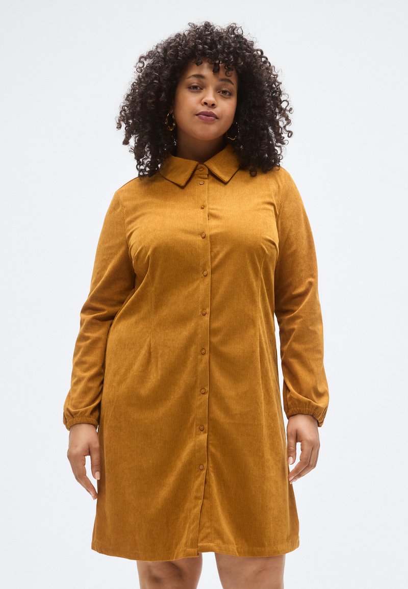 Sennepsgul kordfløyelskjortedress med krage, knapper foran og lange ermer med elastiske mansjetter. Har en avslappet passform og lett tekstur.