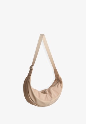 Sac à dos en toile beige en forme de croissant, doté d'une bandoulière réglable et d'un zip pour une fermeture sécurisée. Texture lisse.