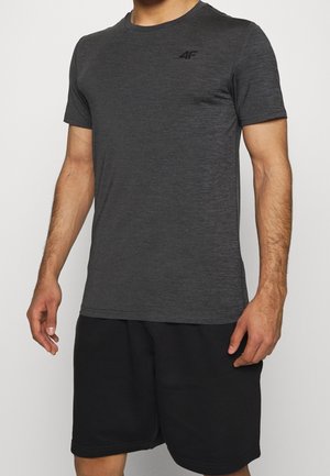 Mand iført en mørkegrå atletisk kortærmet skjorte og sorte shorts, stående mod en ensartet lys baggrund.