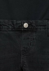 Close-up of black denim jeans waistband with silver button and visible stitching against a black fabric background.