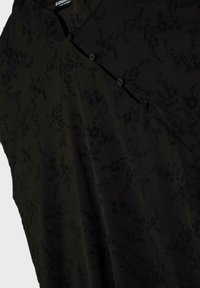 Tissu noir avec un motif floral subtil et une fermeture diagonale à boutons près d'un col rond.