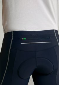 Shorts de sport navy avec une poche arrière zippée dotée d'une languette verte, des accents réfléchissants et un domaine rembourré pour le confort.
