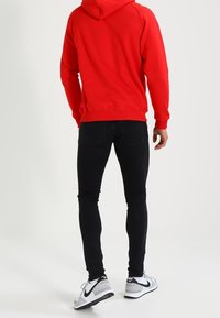 Červená mikina s klokaní kapsou, černé úzké džíny a šedé tenisky s černými detaily. Hladká tkanina a přiléhavý střih.