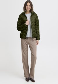 Alyvuogių žalios spalvos pūkinė striukė su chevrono siūlėmis, kapišonu ir užtrauktuku priekyje; derinama su šviesiai pilka palaidine ir smėlio spalvos kelnėmis.