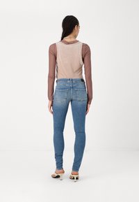 Modré skinny džíny s vysokým pasem a vybledlým umytím, se zadními kapsami, kombinované s světle růžovým topem bez rukávů a otevřenou špičkou.