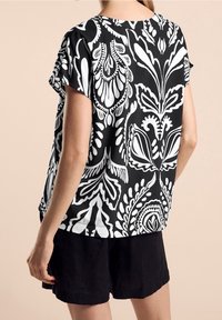 Svart och vit kortärmad topp med ett djärvt blommönster. Lätt och luftig passform med rund halsringning, tillverkad av lättviktsmaterial.