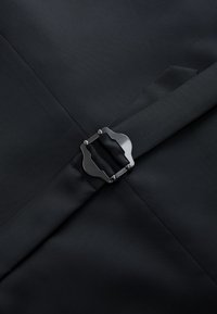 Cinturón de tela negra con hebilla metálica negra mate asegurada sobre tela negra lisa con costuras visibles.