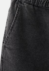 Zbliżenie na czarny materiał dżinsowy, pokazujący przednią kieszeń z widocznym szwem i marszczoną talię.