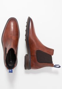 Bottes courtes en cuir marron avec des panneaux latéraux élastiques, un bout arrondi et une semelle en caoutchouc texturée. Équipées d'une languette bleue pour un enfilage facile.